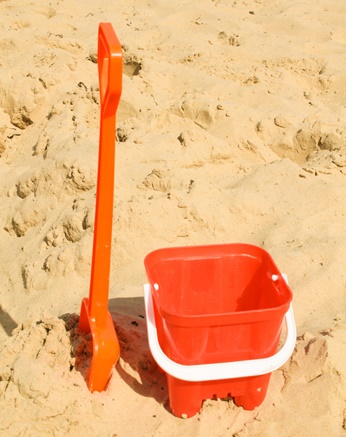Red plastic bucket and spade in the sand